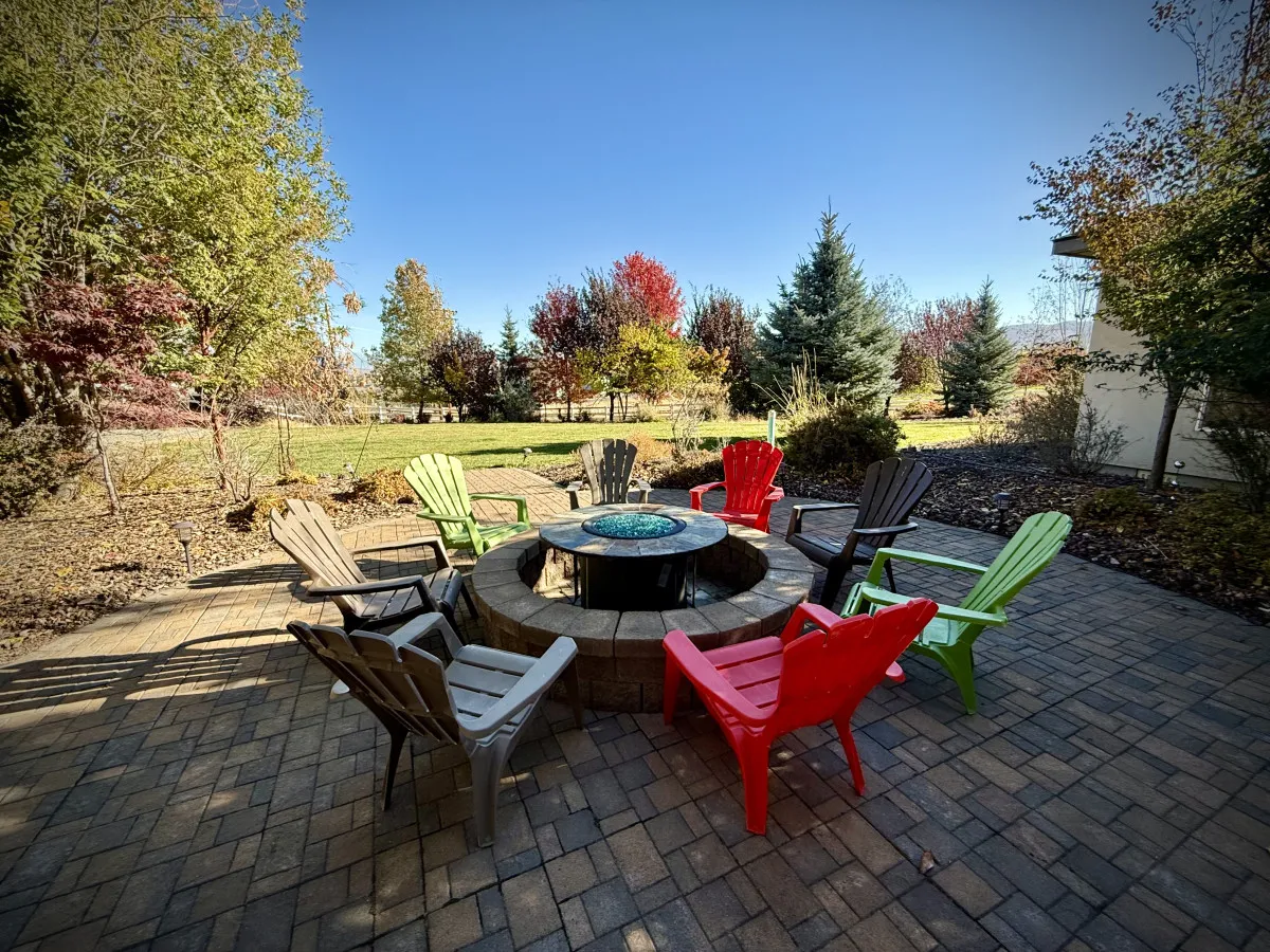 An inviting outdoor fire pit area with colorful chairs and a landscaped garden. The space is set for gathering, with a cozy and communal mood that encourages relaxing or sharing treats in the evening.