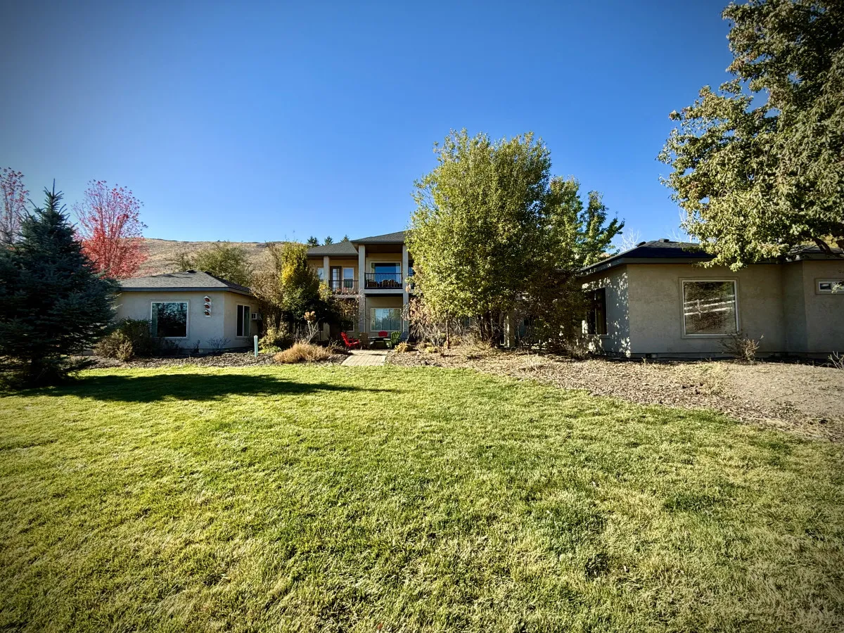 This image shows a welcoming two-story house surrounded by a landscaped yard and a variety of mature trees. The expansive outdoor space features a balcony view and ample lawn area, perfect for group activities like barbecues or lawn games. The image radiates a serene, inviting atmosphere ideal for gatherings.