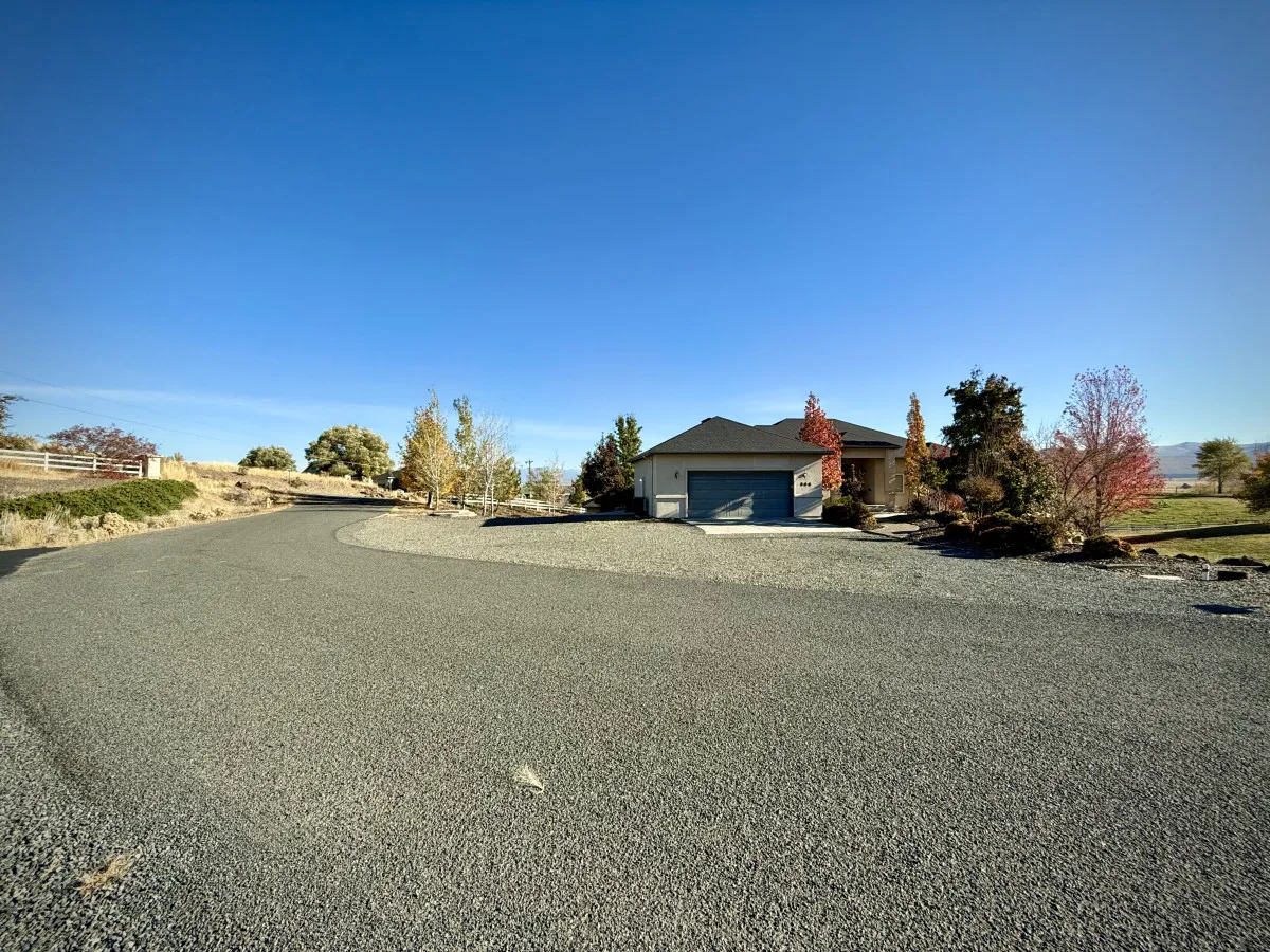 A serene view of the house exterior, surrounded by trees and a spacious yard, suggesting privacy and tranquility. The open grassy space is ideal for peaceful walks or moments by the firepit, catering to guests traveling with pets.
