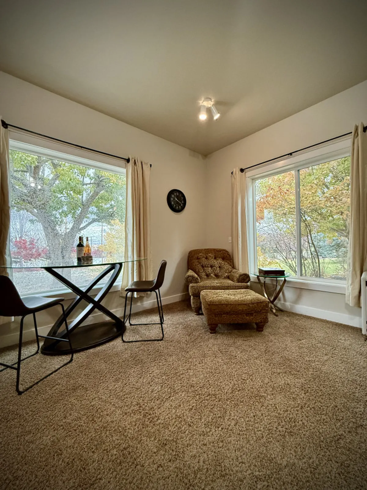 A cozy interior dining area with a glass table, comfortable armchair, and large windows framing lush outdoor views. The natural light streaming in makes the space feel inviting—perfect for enjoying breakfast or coffee in the morning.